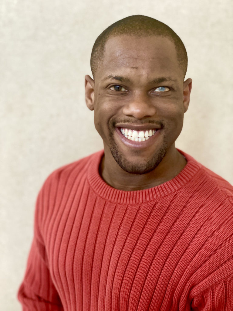 Image Description: Headshot of Telephone artist Davian Robinson. He is smiling and wears a red sweater and is in front of a light background. 